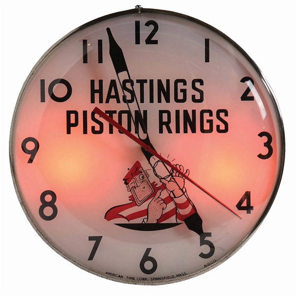 HASTINGS PISTON RINGS GLASS FACE LIGHT UP SERVICE STATION CLOCK.