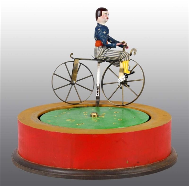 COMPOSITION BICYCLIST TOY RIDING ON ROUND BASE.   