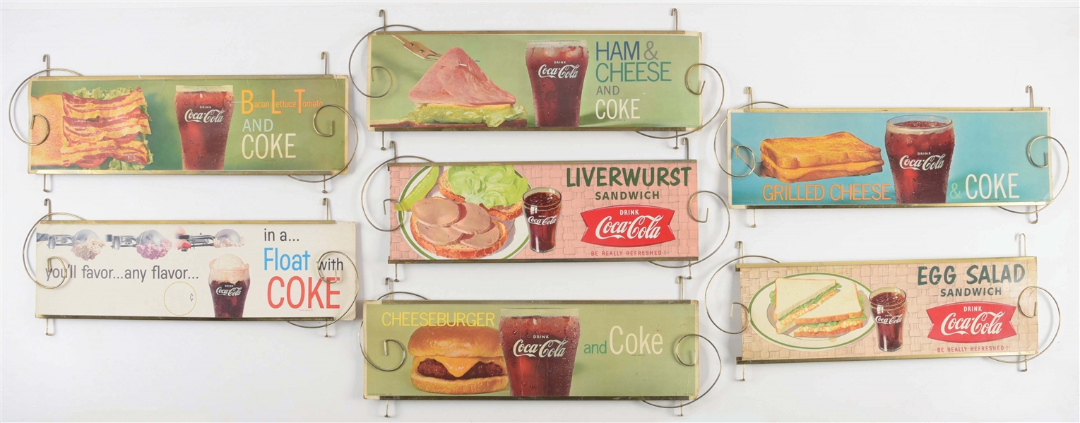COLLECTION OF 7 COCA-COLA CARDBOARD LITHOGRAPH CHANNEL SIGNS W/ ORIGINAL METAL DISPLAYS.